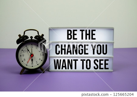 Be the change you want to see text on LED lightbox with alarm clock on purple background 125665204