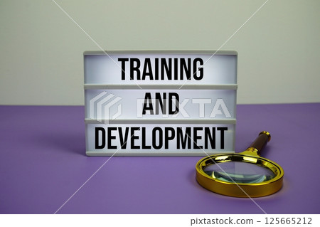 Training and Development text on LED lightbox with magnifying glass on purple background 125665212