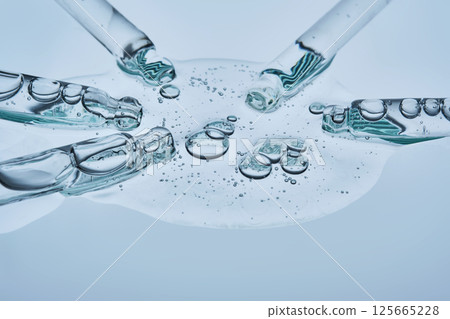 A large drop of hyaluronic serum for a blistered face and several pipettes on a blue background. A large drop of hyaluronic serum for a blistered face and several pipettes on a blue background. 125665228