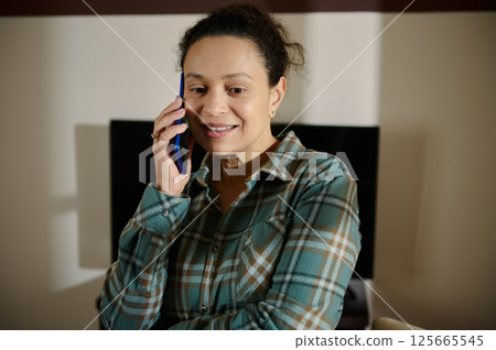 Smiling Woman Talking on Smartphone in Cozy Indoor Setting Smiling Woman Talking on Smartphone in Cozy Indoor Setting 125665545