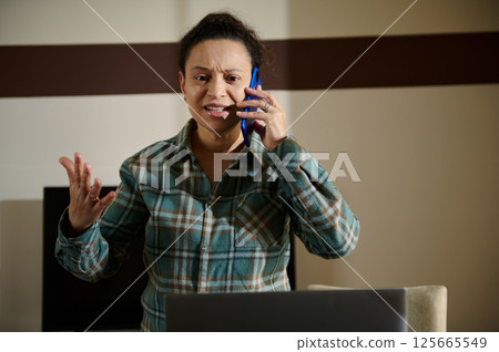 Woman Expressing Frustration While on a Phone Call in Home Office Setting Woman Expressing Frustration While on a Phone Call in Home Office Setting 125665549