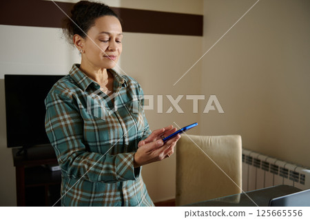 Woman Using Smartphone in a Bright Home Interior Setting Woman Using Smartphone in a Bright Home Interior Setting 125665556