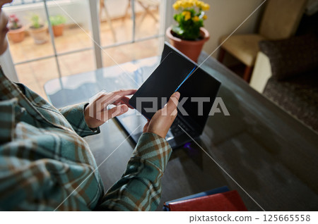Person Using Smartphone Near Laptop in Cozy Home Office Environment 125665558