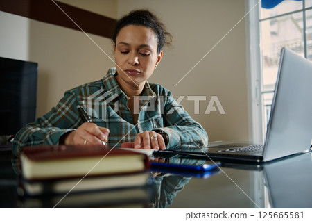 Woman Working on Laptop and Notes in Home Office Setting 125665581