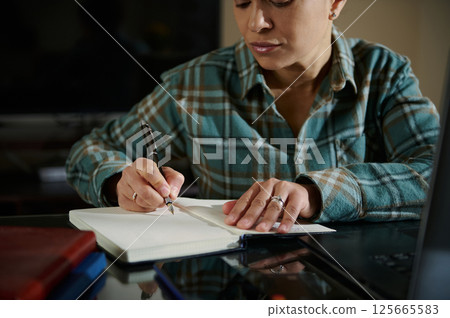 Focused Woman Writing Notes in a Journal at Her Desk Focused Woman Writing Notes in a Journal at Her Desk 125665583