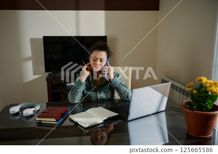 Woman Multitasking with Laptop and Phone in Home Office Environment 125665586