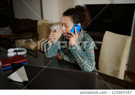Woman Working From Home Office on Phone and Planning on Laptop Woman Working From Home Office on Phone and Planning on Laptop 125665587