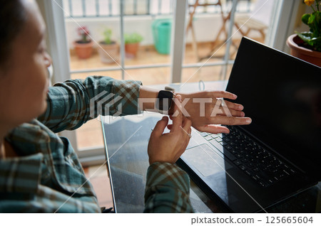 Person Using Smartwatch While Working on Laptop at Home Office Person Using Smartwatch While Working on Laptop at Home Office 125665604
