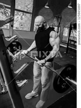 A very strong man (trainer?) is doing biceps exercises in a gym 125665897
