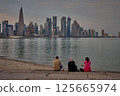 Doha Qatar skyline from corniche promenade sunset shot showing dhows in Arabic gulf with Qatar flag and people sitting Doha Qatar skyline from corniche promenade sunset shot showing dhows in Arabic gulf with Qatar flag and people sitting 125665974