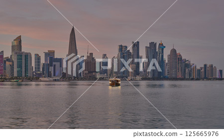 Doha Qatar skyline from corniche promenade sunset shot showing dhows in Arabic gulf with Qatar flag 125665976