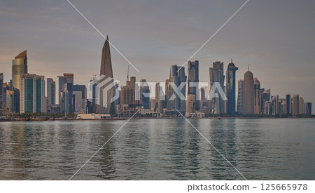 Doha Qatar skyline from corniche promenade sunset shot showing dhows in Arabic gulf with Qatar flag 125665978