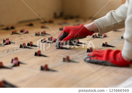 Man Installing Tile Leveling System Components on The Tiled Floor. Man Installing Tile Leveling System Components on The Tiled Floor. 125666569