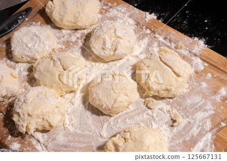 Irregularly shaped dough pieces dusted with flour rest on a wooden surface, ready for baking or cooking. Irregularly shaped dough pieces dusted with flour rest on a wooden surface, ready for baking or cooking. 125667131