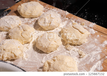 Irregularly shaped dough pieces dusted with flour rest on a wooden surface, ready for baking or cooking. 125667132