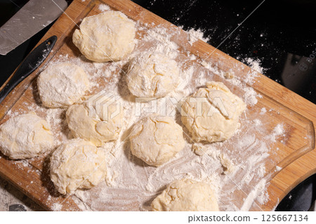 Irregularly shaped dough pieces dusted with flour rest on a wooden surface, ready for baking or cooking. Irregularly shaped dough pieces dusted with flour rest on a wooden surface, ready for baking or cooking. 125667134