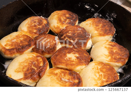 Golden brown pieces of fried dough sizzle in a black skillet, glistening with oil. Golden brown pieces of fried dough sizzle in a black skillet, glistening with oil. 125667137