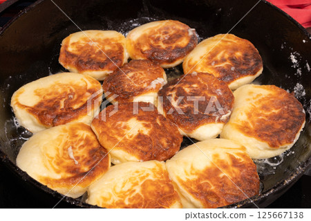 Golden brown pieces of fried dough sizzle in a black skillet, glistening with oil. Golden brown pieces of fried dough sizzle in a black skillet, glistening with oil. 125667138