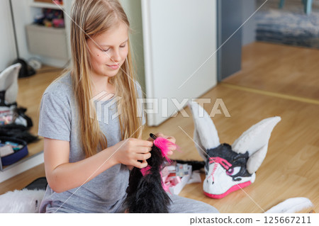 Cute teenager girl blonde hair sits floor sewing pink black fur costume piece. Child making homemade furry dragon mask. Quadrobic Therian fandom subculture. Design hobby creative artwork 125667211