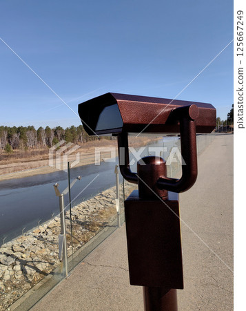binoculars placed beside calm river, inviting viewers to observe nature in peaceful surroundings. 125667249