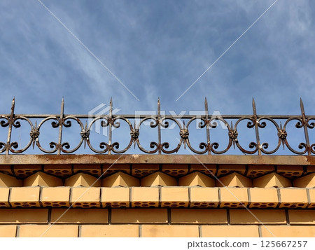 decorative brick fence intricate metal decoration against clear blue sky. close up. decorative brick fence intricate metal decoration against clear blue sky. close up. 125667257