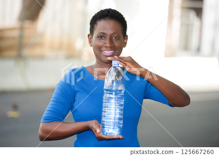 young happy woman holding a bottle of mineral water in town 125667260