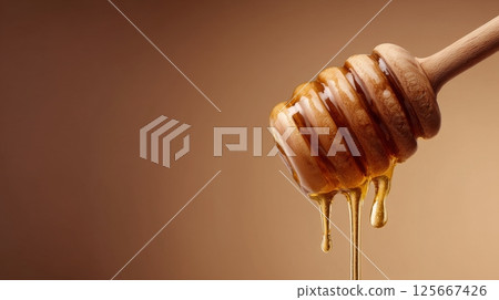 Honey dipper with golden liquid honey against a brown background 125667426