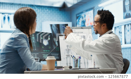 General practitioner examining x ray scan test results with patient, giving the right diagnostic report in medical cabinet. Doctor reviews analysis on health insurance, medical technology. Camera A. General practitioner examining x ray scan test results with patient, giving the right diagnostic report in medical cabinet. Doctor reviews analysis on health insurance, medical technology. Camera A. 125667877