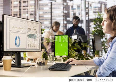 Professional employee works at desk with green screen in a corporation, working on financial planning and business strategy. Focused woman manages company development, networking. Professional employee works at desk with green screen in a corporation, working on financial planning and business strategy. Focused woman manages company development, networking. 125667985