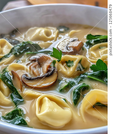 Tortellini soup with mushroom and spinach in creamy broth, a delicious Italian meal 125668479