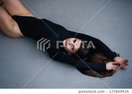 Beautiful slim brunette woman with perfect body in black bodysuit posing on grey studio background. Beautiful slim brunette woman with perfect body in black bodysuit posing on grey studio background. 125669426
