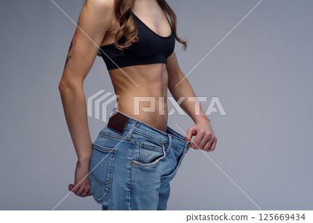 Woman with perfect body demonstrates weight loss, slimming by wearing old big jeans 125669434