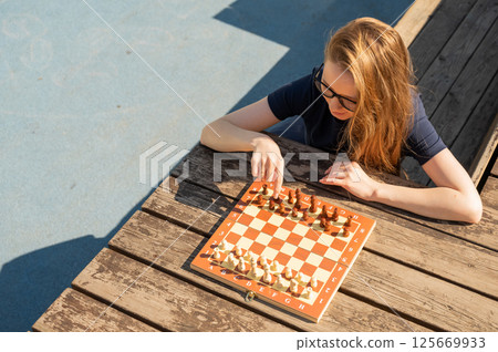 Caucasian woman playing chess outdoors. Caucasian woman playing chess outdoors. 125669933