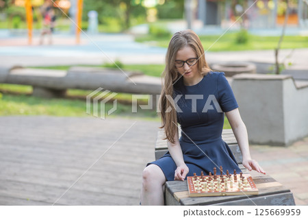 Caucasian woman playing chess outdoors. Caucasian woman playing chess outdoors. 125669959