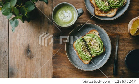 Top-down shot of two avocado toasts on gray plates, a matcha latte, and a knife on a textured wooden table. Healthy brunch setting with plant AI generated 125670247