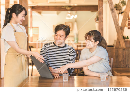 A clerk explaining a man and a woman who order and self-order a menu using a tablet at a cafe, restaurant, or restaurant 125670286