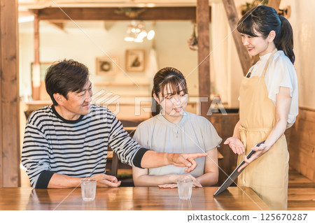A clerk explaining a man and a woman who order and self-order a menu using a tablet at a cafe, restaurant, or restaurant 125670287