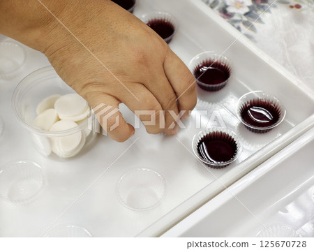A woman's hands are preparing bread and grape juice for the Holy Communion ceremony. 125670728