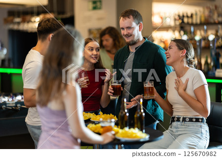 Happy mens and womens drinking beer and eating crisps, laughing and spending time together in bar Happy mens and womens drinking beer and eating crisps, laughing and spending time together in bar 125670982