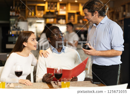 Waiter helping couple choose food and wine at restaurant 125671035