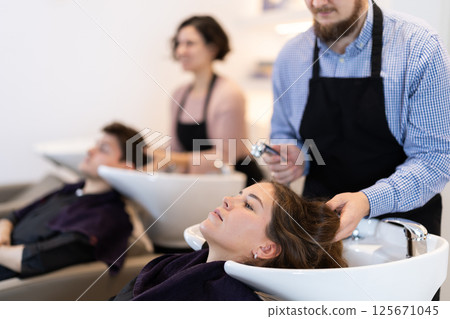 Young male hairdresser washing hair of female client Young male hairdresser washing hair of female client 125671045