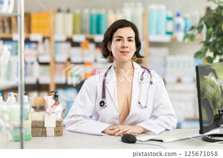 Female pharmacist in unbuttoned gown invites to pharmacy 125671058