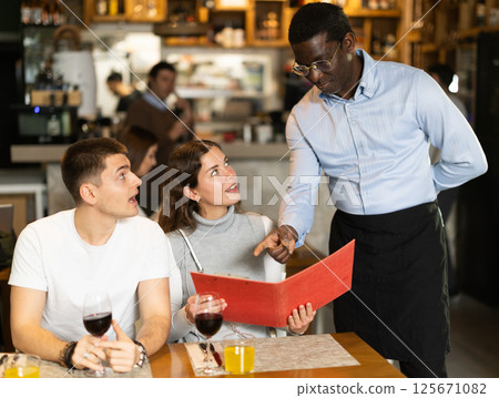 African man listen to restaurant couple customer, writes down order 125671082
