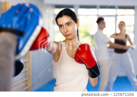 Young girl training boxing kicks on punch mitts held by instructor 125671108