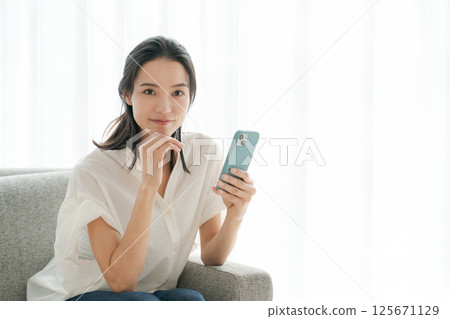 一位 30 多歲的女性正在家中操作智慧型手機 125671129