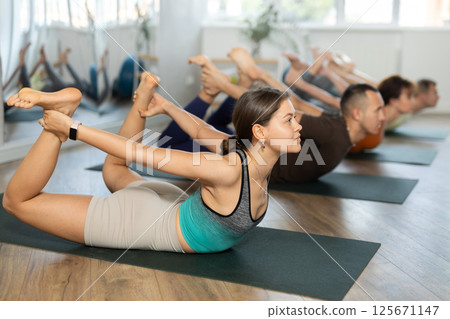 Lovers of active lifestyle on yoga mat perform doing dhanurasana in gym 125671147