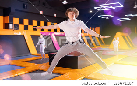 Portrait of joyful young teenager in sport clothes enjoying weekend time on trampolines in entertainment center 125671194