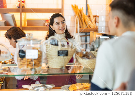 Young woman giving pastry to customer in cafe 125671198