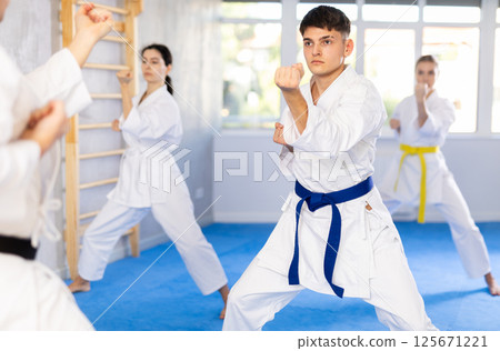 Middle-aged man attendee of karate classes practicing kata standing in row with others 125671221