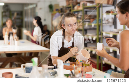 Young man sits near table and decorates clay ceramic craft vase, plate 125671223